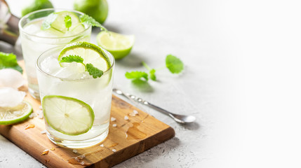 Cold refreshing drink in a glass with slices of lime, mint and ice cubes, free space for text. Summer lemonade with citrus close-up, copy space.