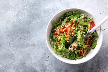 The concept of healthy food. Leaf salad with grits and pine nuts in a deep bowl. Arugula, spinach, tomatoes, spelt on a light background. Background image, copy space