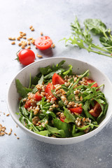 The concept of healthy food. Leaf salad with grits and pine nuts in a deep bowl. Arugula, spinach, tomatoes, spelt on a light background. Background image, copy space