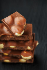 Chocolate with hazelnut in the form of a tower on a dark background. Pieces of milk chocolate with nuts.