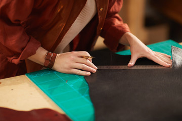 Unrecognizable female artisan measuring piece of dark brown leather to cut it out, horizontal shot