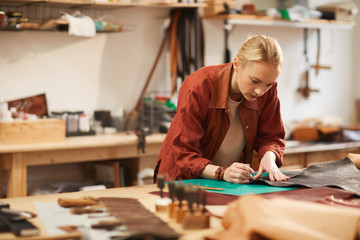 Fototapeta premium Horizontal portrait of young Caucasian craftswoman creating something using piece of leather