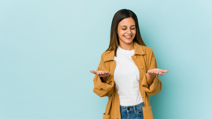 Young woman isolated on blue background holding something with palms, offering to camera.