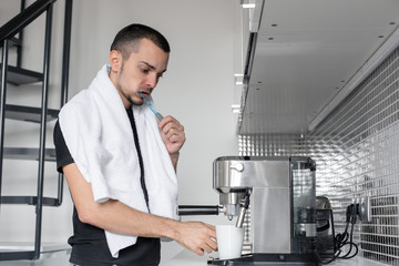 A young guy is going to work in the morning. Brushes teeth near a coffee machine while waiting for a cup of coffee