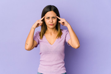 Young woman isolated on purple background focused on a task, keeping forefingers pointing head.