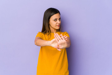 Young woman isolated on purple background standing with outstretched hand showing stop sign, preventing you.