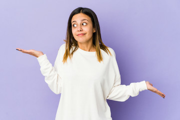 Young woman isolated on purple background confused and doubtful shrugging shoulders to hold a copy...
