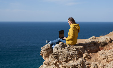A freelancer girl is working typing on a laptop and looking at a monitor with a beautiful view of the open air sea sky. Traveling with a computer. Online dream job.