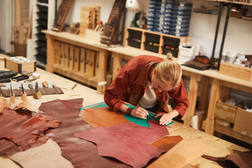Horizontal high angle shot of modern young woman working in leather craft workshop, copy space