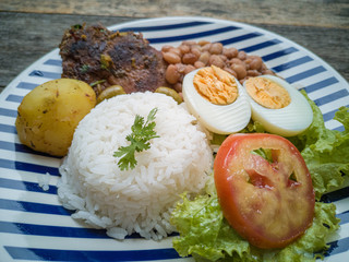 Food dish. Beans, rice, meat, salad, egg. Rustic wood background.