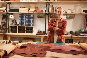 Horizontal shot of cheerful young Caucasian woman standing in her workshop with arms crossed looking at camera smiling