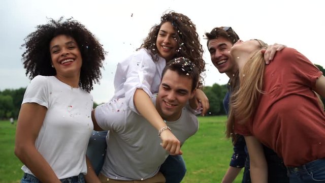 Group of four friends having fun at the park blowing confetti - Millennials playing together at sunset