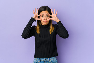 Young woman isolated on purple background keeping eyes opened to find a success opportunity.