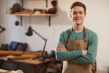 Horizontal medium portrait of young Caucasian craftsman wearing apron standing with arms crossed looking at camera smiling - Powered by Adobe