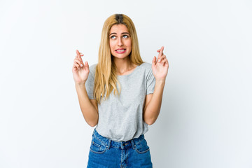 Young blonde woman isolated on white background crossing fingers for having luck