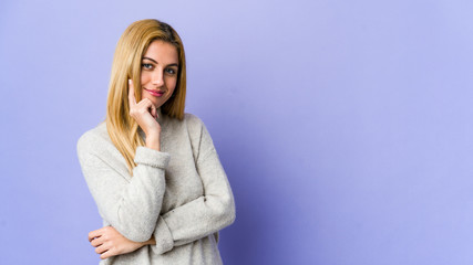 Young blonde woman isolated on purple background smiling happy and confident, touching chin with hand.