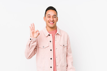 Young latin man posing isolated cheerful and confident showing ok gesture.