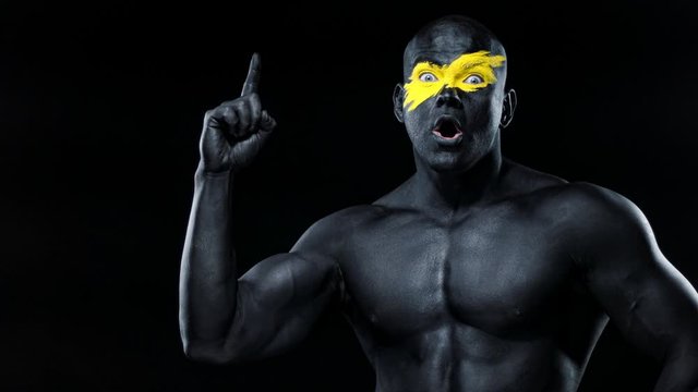 Man have a good idea. Bodybuilder athlete with yellow face art and black body paint. Colorful portrait of the guy with bodyart.