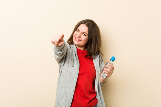 Young Plus Size Curvy Woman Holding A Water Bottle Cheerful Smiles Pointing To Front.