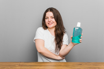 Young plus size curvy woman holding a mouthwash smiling confident with crossed arms.