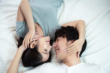 Obraz na płótnie Canvas close up portrait of pretty young asian couple with happiness. asia man and woman lay on bed facing together with big smile hand touch face,love emotion with valentine concept .