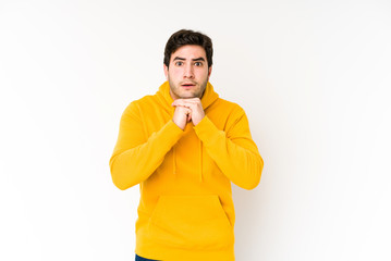 Young man isolated on white background praying for luck, amazed and opening mouth looking to front.