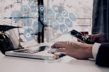 Hands of business people using smartphone and laptop with network interface icons on office table. Double exposure Concept.	