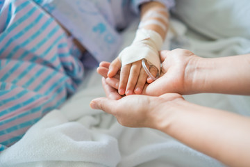 Little girl was sick and her hand was hold by her mother in hospital room. Selective focus,