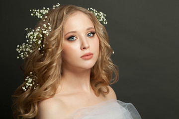 Attractive blonde model girl with long healthy curly hair and white flowers on dark background