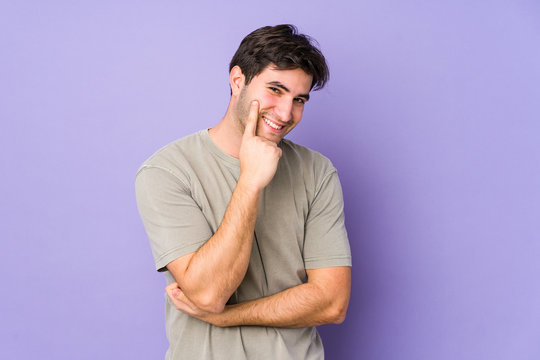 Young man isolated on purple background smiling happy and confident, touching chin with hand.