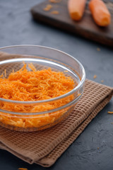 Juicy and fresh grated carrots on a wooden board on a dark background