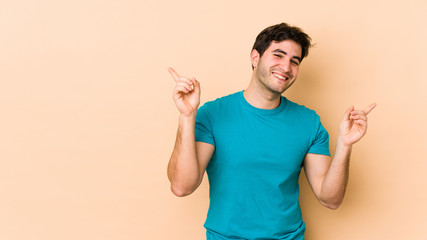 Young man isolated on beige background pointing to different copy spaces, choosing one of them, showing with finger.