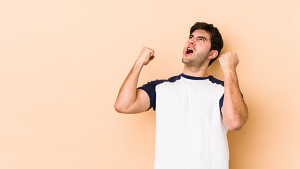 Young man isolated on beige background raising fist after a victory, winner concept.