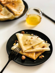 Crepes with honey and nuts, on a white plate, in black dishes. Homemade thin pancakes for breakfast or dessert.
