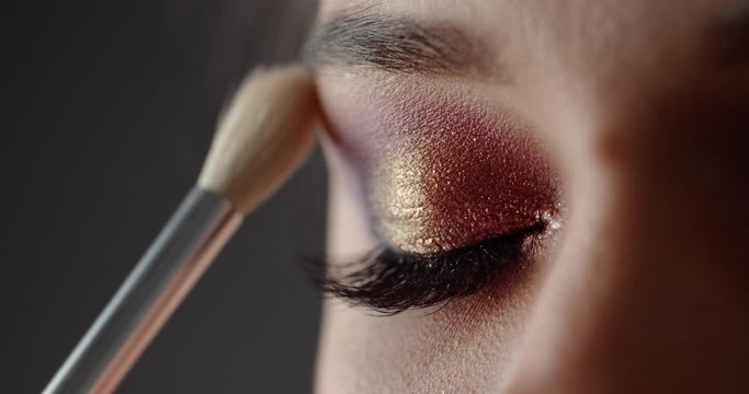 Makeup artist applying colorful eyeshadow on model's eye using professional brush. Extreme close up. Concept of beauty and style.