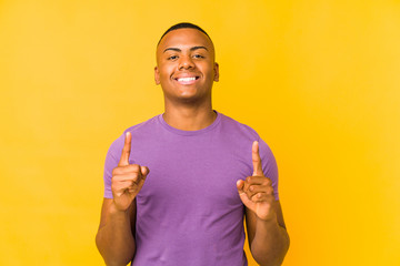 Young latin man isolated on yellow background indicates with both fore fingers up showing a blank...