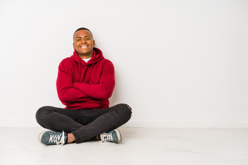 Young latin man sitting on the floor isolated who feels confident, crossing arms with determination.