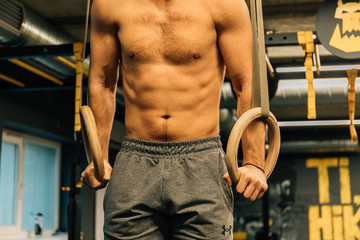 Naklejka premium Muscle up exercise athletic man doing intense workout at the gym on gymnastic rings. Fitness, sport and healthy lifestyle concept.