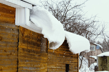 A large white pile of snow hanging from the roof of a house. Close-up. Background. Scenery.