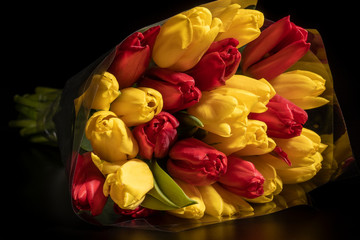 Bouquet of spring tulip flowers in a wrapping wrapper in red and yellow on a black background