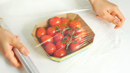 Woman using food film for food storage on a white table. Roll of transparent polyethylene food film for packing products.