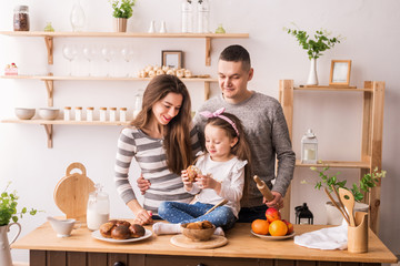 Obraz na płótnie Canvas A cute little girl and her beautiful parents prepare food and smile while cooking in the kitchen at home. Knead the dough on pancakes and rolls