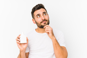 Young caucasian man holding a vitamins bottle isolated looking sideways with doubtful and skeptical expression.