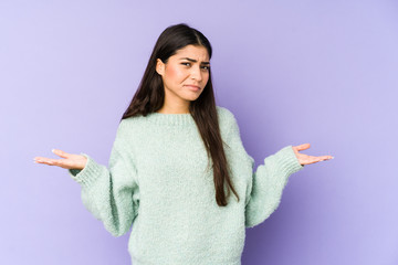 Young indian woman isolated on purple background doubting and shrugging shoulders in questioning...