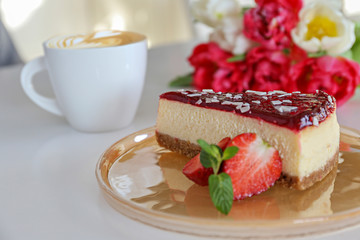 Delicious healthy vegetarian food, organic strawberry cheesecake slice, fresh red berries, green mint leaves, bouquet of different tulips and cup of cappuccino on white table. Close up, top front view