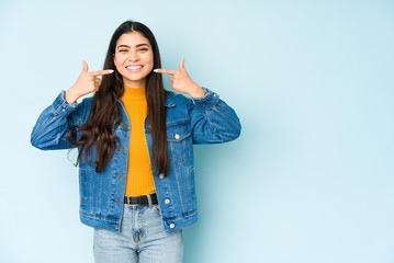 Young indian woman isolated on blue background smiles, pointing fingers at mouth.