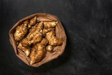 Several Jerusalem artichoke tubers in a paper bag on a black background with copy space. Helianthus tuberosus. Top view