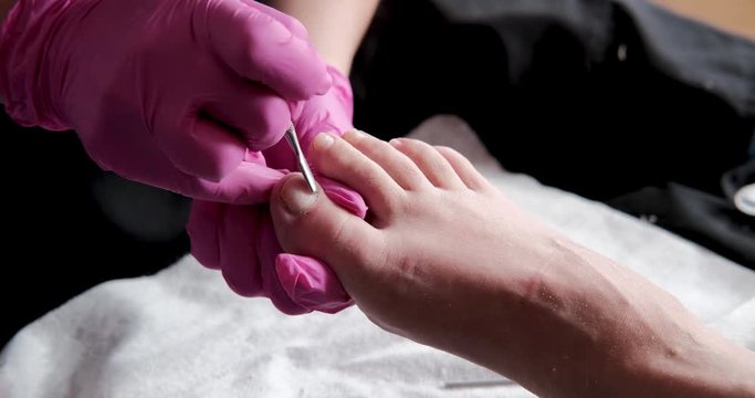 Pedicurist master in pink gloves is cuts the cuticle and shellac toe nails in the pedicure salon using drill.  Professional pedicure in cosmetology clinic. Hygiene for feet in beauty salon.