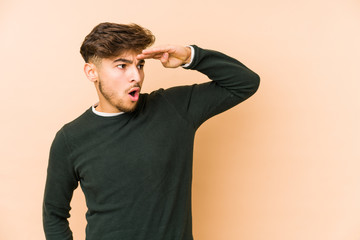 Young arabian man isolated on a beige background looking far away keeping hand on forehead.