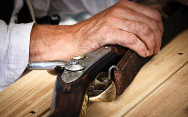 An old vintage rifle hold  by a mans arm on a wooden table.